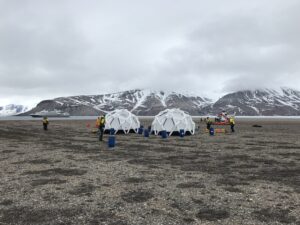 Beach in Svalbard with two emergency shelter tents and people.